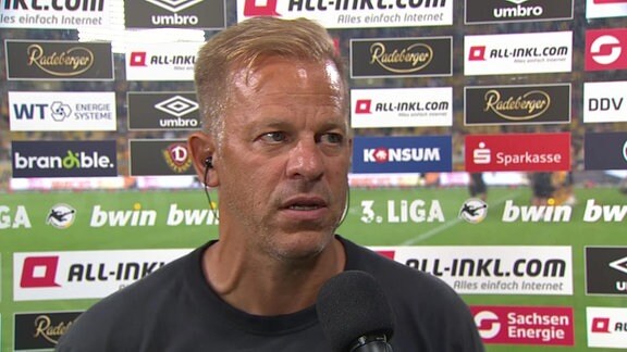 Dynamo Dresdens Trainer Markus Anfang vor einer Werbetafel am Mikrofon