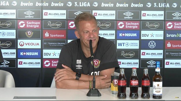 Dynamo Dresdens Trainer Markus Anfang bei der Pressekonferenz vor einer Werbetafel am Mikrofon
