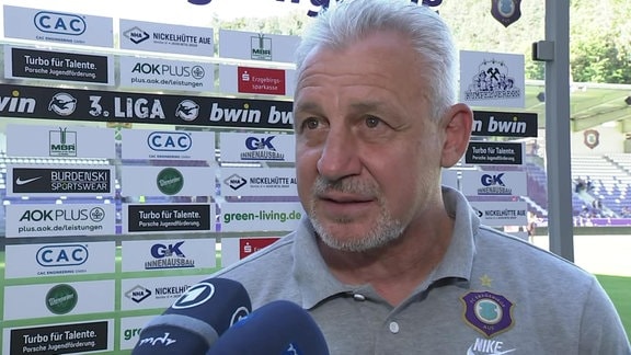 Aue-Coach Pavel Dotchev im Interview vor einer Werbebande im Stadion