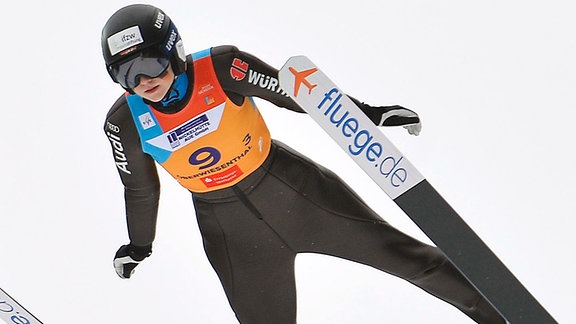 Skispringerin im Flug auf Skiern mit Aufschrift fluege.de