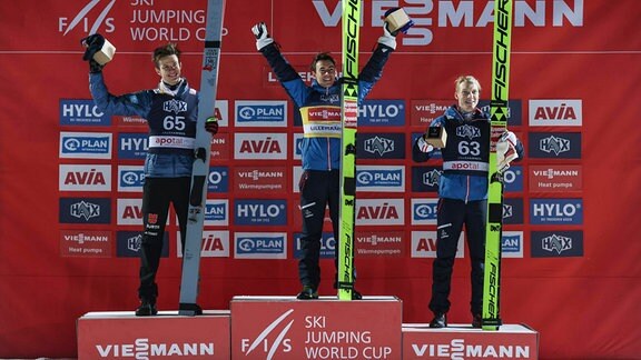 Drei Skispringer jubeln auf den Siegertreppchen.