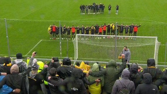 Fussballer stehen in einer Reihe vor ihren Fans.