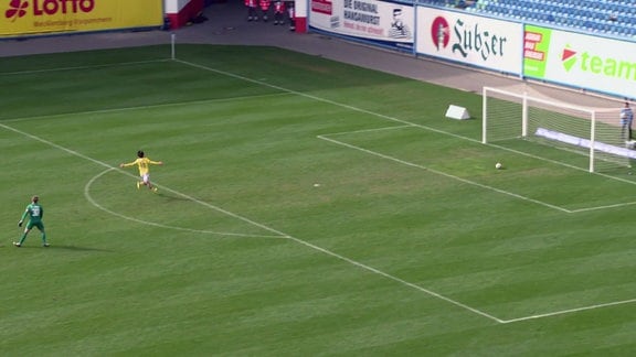 Spieler von Jena spielt den Ball am Torwart vorbei und jubelt während der Ball auf das Tor zurollt.