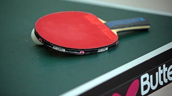 Tischtennis-Schläger und -Ball liegen auf einer Tischtennisplatte.