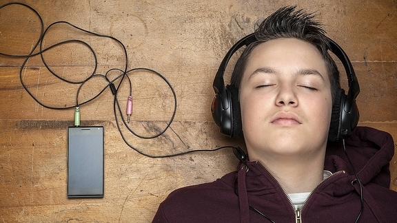 Ein Junge hat Kopfhörer auf und hört mit geschlossenen Augen.