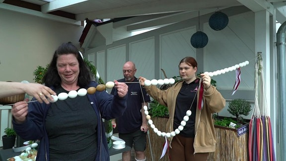 Zwei Frauen und ein Mann bereiten Eiergirlanden für einen Festumzug in Heiligenstadt vor.