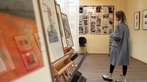 Eine junge Frau in der Ausstellung zur Ukraine, es hängen Bilder und andere Informationen an den Wänden.