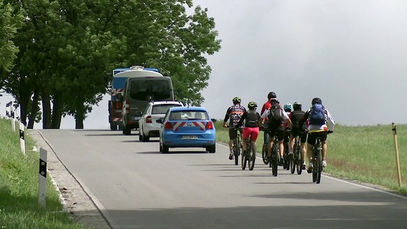 Autos und eine Gruppe Radfahrer auf einer Landstraße.