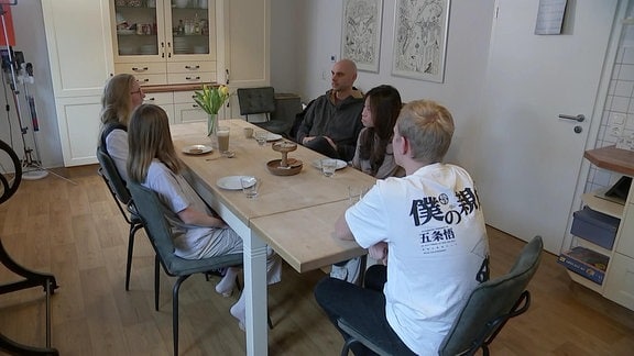 Eine Austauschschülerin sitzt mit ihrer Gastfamilie am Tisch.