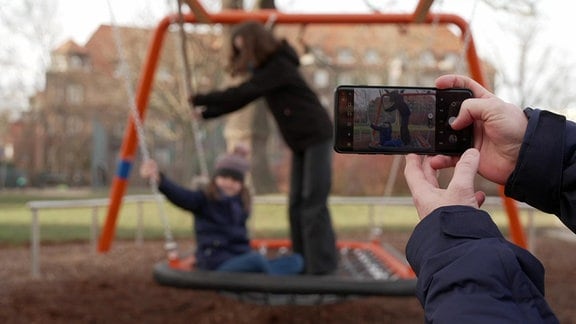 Ein Mann fotografiert zwei Kinder auf einem Spielplatz.