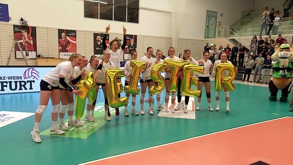 Volleyballerinnen halten Buchstabenluftballons, die das Wort "Meister" bilden, vor sich