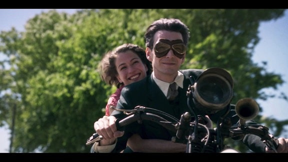 Filmausschnitt: Mann und Frau auf einem Motorrad