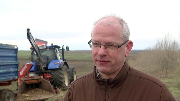 Ein Landwirt vor einem Feld, auf dem ein Traktor steht