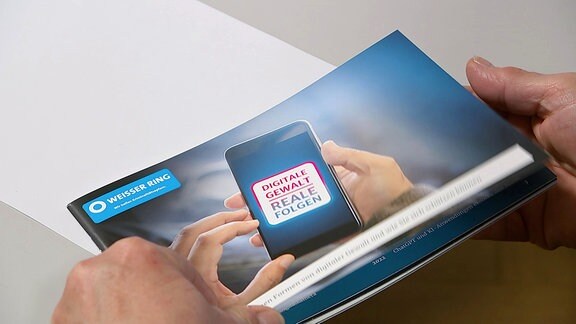 zwei Hände halten eine Broschüre des Weißen Ringes zu Digitaler Gewalt