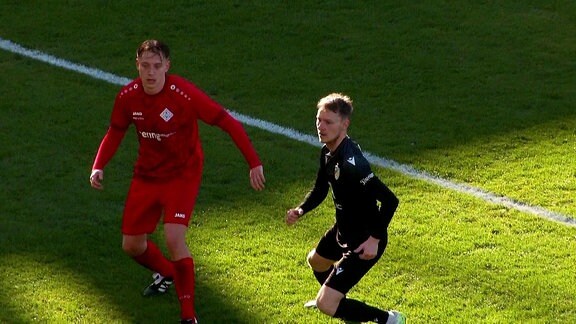 Ein Fußballer von Schott Jena läuft neben einem Spieler vom FC Carl Zeiss Jena auf dem Fußballfeld