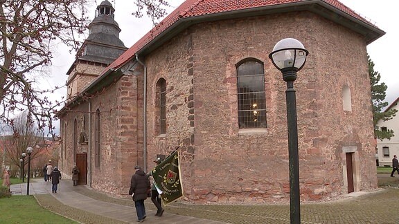Die Pfarrkriche St. Marien in Niederorschel von außen, davor zwei Menschen mit einer Fahne