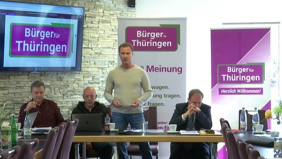 Vier Menschen in einem Raum vor Aufstellern mit dem Schriftzug "Bürger für Thüringen"