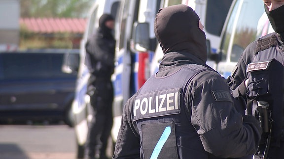 Polizist in Einsatzmontur vor mehreren Polizeiautos 
