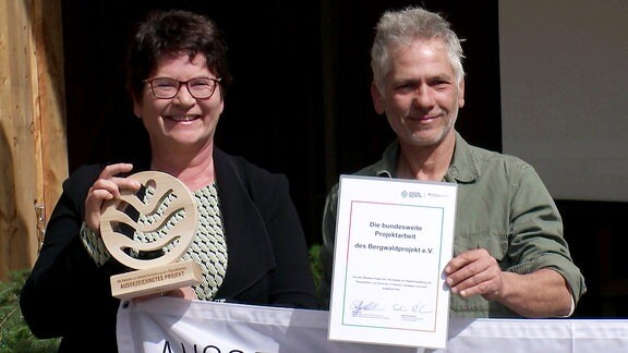 Ein Mann und eine Frau halten den Preis und die Urkunde als "Herausragendes UN-Dekade-Projekt" in den Händen 
