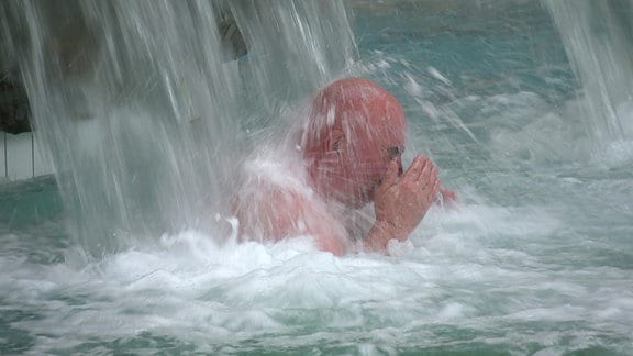 Ein Mann steht in einem Schwimmbecken unter einem Wasserfall