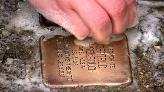 Eine Hand putzt im Rahmen einer gemeinnützigen Aktion Stolpersteine in Weimar