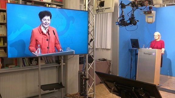 Ein großer Bildschirm mit Thüringens Finanzministerin Heike Taubert, im Hintergrund eine Frau an einem Pult