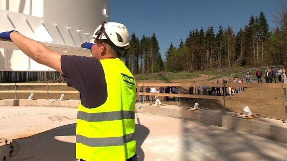 Ein Bauarbeiter mit Signalweste und Helm sichert ein Bauteil aus Metall