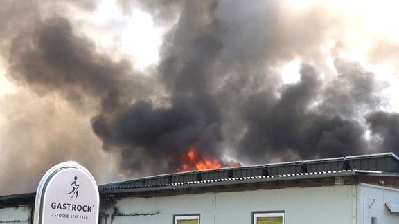 Flammen und Rauch auf dem Dach eines Gebäudes, davor das Unternehmensschild "Gastrock"