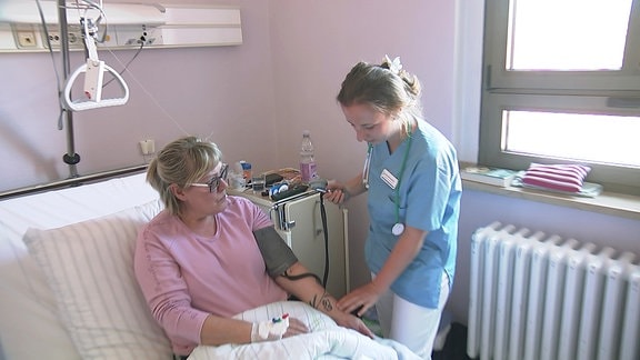 Pflegekraft steht neben Frau in einem Krankenhausbett