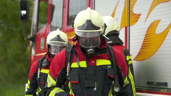 Drei Feuerwehrmänner mit Atemschutz neben einem Feuerwehrauto