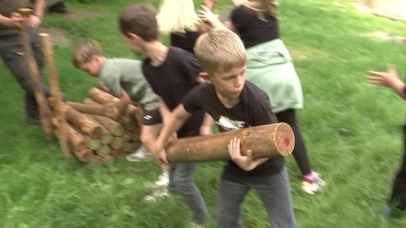 Kinder tragen kurze Baumstämme im Wald