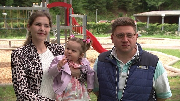 eine ukrainische Familie mit Vater, Mutter und einem Kleinkind auf einem Spielplatz