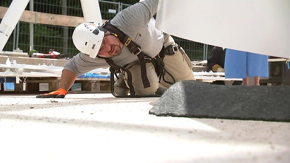 Ein Arbeiter kniet auf dem Boden und schaut, dass ein schweres Metallteil exakt eingesetzt wird