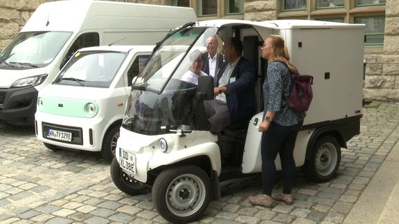 vier Menschen schauen sich ein kleines Elektro-Lieferfahrzeug an 