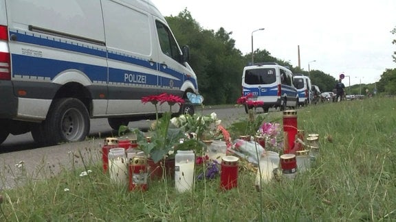 Kerzen am Tatort vor Polizeiautos im Hintergrund 