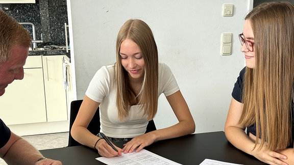 Eine junge Frau unterschreibt einen Ausbildungsvertrag