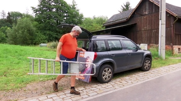 Mann trägt Leiter und Wahlplakat