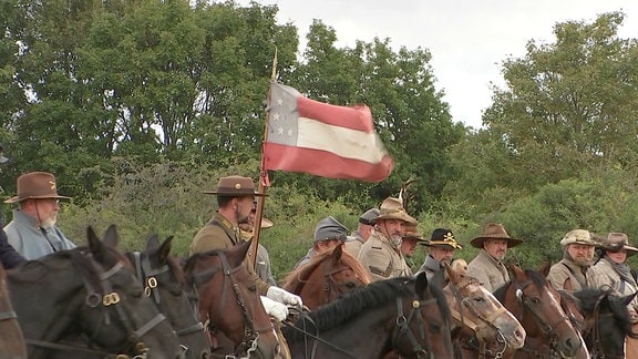 Darsteller mit Uniformen aus dem US-Bürgerkrieg, Pferden und einer Fahne