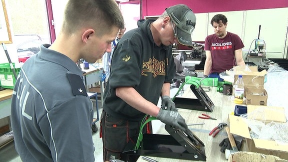 Ein Mitarbeiter vom Zoll und ein andere Mann arbeiten gemeinsam in einer Metallwerkstatt