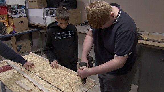Zwei Jungen bauen eine Kiste aus Holz.