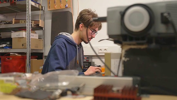 Ein junger Mann  mit Brille an einer Maschine