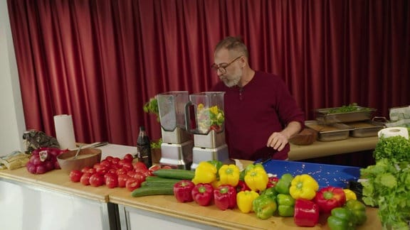 Ein Mann steht hinter mit Gemüse beladenen Tischen.