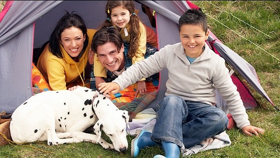 Eine Familie sitzt an einem Zelt und der Hund liegt vor ihnen.