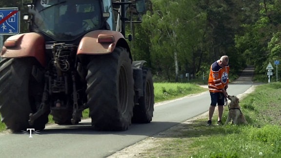 Hund Eddie mit seinem Herrchen neben einer Straße, auf der ein Traktor angefahren kommt