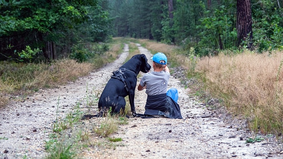 Ein Hund sitzt neben einem kleinen Jungen auf einem Waldweg