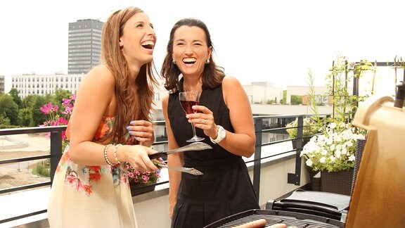 Zwei Frauen grillen auf einem Balkon.