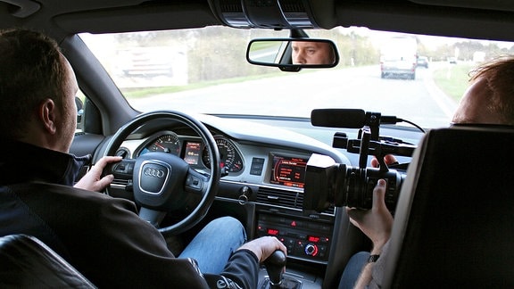 Ein Kameramann filmt Volker Barth beim Autofahren.