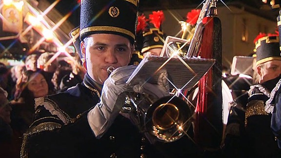 Ein Bergmann spiel bei weihnachtlichem Lichterglanz in seine Trompete