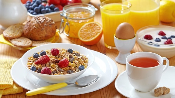 Ein Frühstückstisch mit Müsli, Tee, Brötchen, einem Ei und Quark