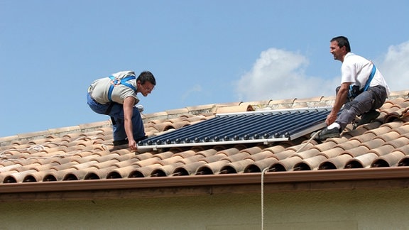 Arbeiter montieren eine Solaranlage auf ein Wohnhaus.
